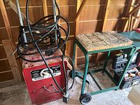 Front view of red welder and green cart side by side in shed