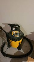 Front angled view of yellow and black Dirt Hawg wet-dry vacuum with attached hose and power cord wrapped on top