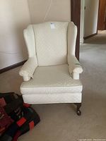 Front view of the cream upholstered wing chair with removable seat cushion and arm covers, showing the Queen Anne wooden legs.