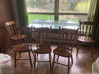 Five matching solid wood chairs arranged in a row near window.
