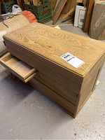 View of wooden box with one drawer pulled out showing drawer construction without knobs and natural wood grain finish.