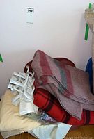 Wool blankets and bedding stacked with white plastic door hooks on top, beside a burgundy storage bin.