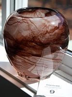 Bulbous violet glass vase with cloudy sepia pattern on windowsill, showing shape and coloration.