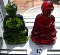 Front view of green and red Buddha figurines side by side on window sill