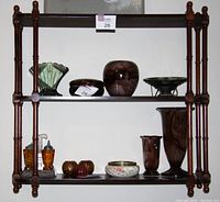 Front view of three-shelf wooden display shelving unit with various decorative items on shelves for scale.