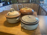 Three ceramic art pottery pieces with lids on wooden kitchen table