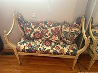 Wood bench shown from a frontal angle, displaying floral upholstered seat and cushions with carved wooden frame.