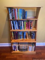 Front view of wooden bookcase filled with various books on four shelves.