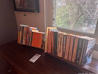 Photo showing two wood book racks holding classic fiction paperbacks including orange Penguin editions.