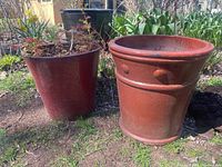 Photo displaying two large ceramic planters side by side outdoors; left planter has live plant, right planter is empty.