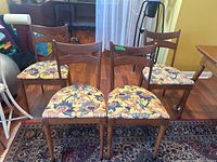 Front view of four side chairs, showing floral upholstered seats and wooden backrests with a horizontal slat.