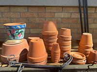 Wide view showing multiple terracotta clay pots in varied sizes, some stacked, with one prominently hand-painted pot.