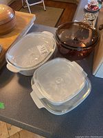 Multiple Corningware and glass casserole dishes and a large brown glass pot with lid on countertop