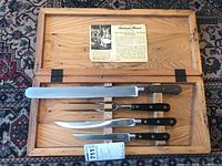 Open wooden case on patterned rug showing four utensils mounted in wood slots
