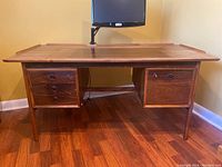 Front view of desk showing walnut veneer top, monitor mount, drawer arrangement and tapered legs