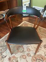 Front view of chair showing wood frame and black vinyl seat and curved backrest.