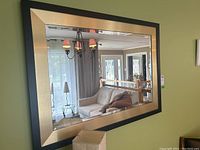 Front view of the rectangular wall mirror showing black outer frame and beveled metallic gold inner frame with clear reflective glass.