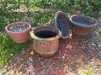 Four planters arranged on ground outdoors, including one terracotta and three dark resin planters
