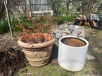 Two resin planters outdoors on grass and near rocks; beige one on left contains live plant, white one on right is empty.