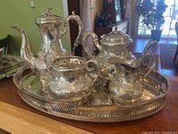 Full tea service lot showing assembled teapot, sugar bowl, creamer, waste bowl on ornate pierced rim tray, all in silver plate with embossed floral decoration