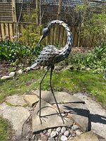 Full front view of steel heron standing on stone patio slabs