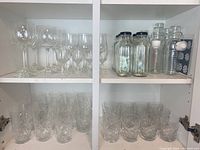 Various glassware displayed on shelves including wine glasses, cocktail glasses, and multiple glass bottles