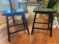 Two black wooden stools positioned on a wood floor with an indoor background.