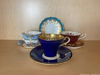 Three matching teacups with saucers arranged side by side, varied colors and gold decorations visible