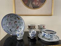 Photo of seven antique Japanese porcelain pieces including large oval plate, lidded cups, small bowls, a matching medium bowl and plate, and a small cup.
