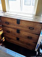 Front view of the antique Japanese clothing chest showing its three drawers with black metal handles and central latches.