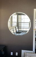 Front view of large round wall mirror mounted on a wall reflecting window blinds and chairs.