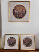 Photo showing three framed Thai warrior paintings hung on a wall. One larger square frame on top with circular painting and two smaller square frames below with circular paintings.
