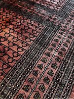 Close-up detail of the Persian rug showing red base tone with black and muted floral and geometric motifs.