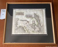 Framed antique map in gold-tone frame hung above wooden surface