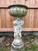 Front view of cement pedestal planter showing fluted bowl and three cupid figures.