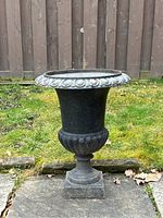 Full frontal view of the black cast iron garden planter placed on stone slab with grass and wooden fence background.
