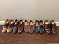 Wide view of all six pairs of men's shoes in size 9 arranged side by side on wooden floor against wall.