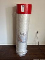 Full view of rolled Solo mattress in packaging showing red top and label.