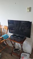 Full view of 32 inch Insignia TV sitting on wooden side table with DVD player beneath and remote control.