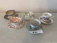 Full view of all five assorted fine china and porcelain teacups and saucers on plain surface