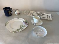 Wide shot of the assorted porcelain and china items showing platter, plates, cup, mug, small figurine, and dish.