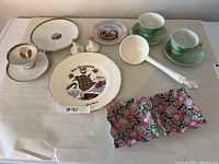 Photo showing assorted porcelain and china items including New Brunswick souvenir plate, cups, saucers, salt and pepper shakers, white ladle, rectangular floral dishes.