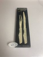 Original packaging image showing the carving set with cream-colored embossed handles and card backing labeled 'Carving Set 2 Piece Stainless Steel'