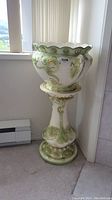Full view of ceramic plant stand showing decorative floral relief in green and white glaze.