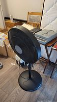 Black ComfortMate standing fan shown from an angle, featuring the circular base and adjustable pole.