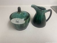 Photo of green ceramic sugar holder with lid next to matching cream pitcher on white surface