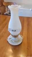 Small vintage desk lamp with white milk glass hobnail shade and base, scalloped edges, brass holder, electrical cord on wooden table.
