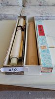 Two Japanese bamboo art scrolls in boxes side by side on a table.