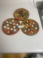 Three woven round cooling pads with dragonfly designs placed on a white countertop.