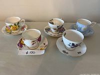 Four Queen Anne fine china teacups and matching saucers, each with a unique floral pattern and gold rim, displayed on a flat surface.